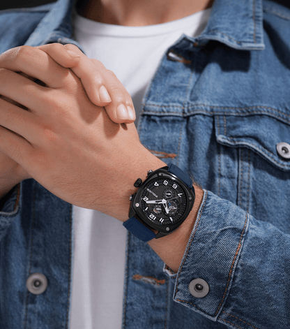 Am Handgelenk getragene Herrenuhr mit dunklem blauem Armband auf Jeanshemd, Ziffernblatt sichtbar.