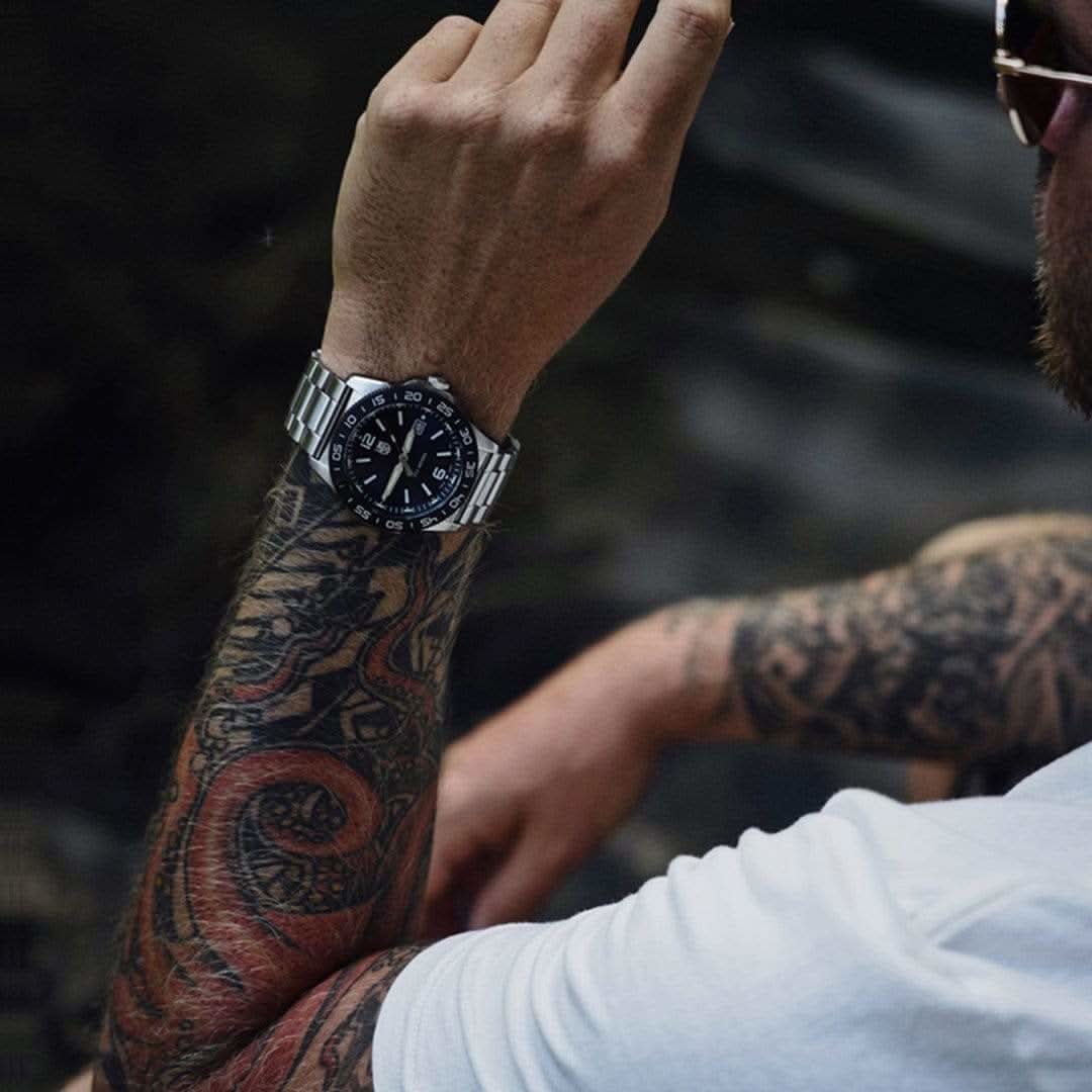 Montre pour homme sur poignet tatoué, cadran noir, bracelet en acier inoxydable