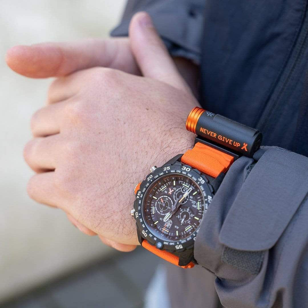 Flash-Taschenlampe am orangefarbenen Uhrenarmband am Handgelenk, schwarzer Korpus.
