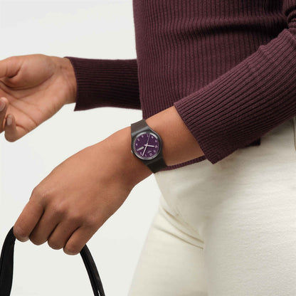 Dunkelbraune Armbanduhr am Handgelenk mit rundem violettem Zifferblatt und „FRI 28“