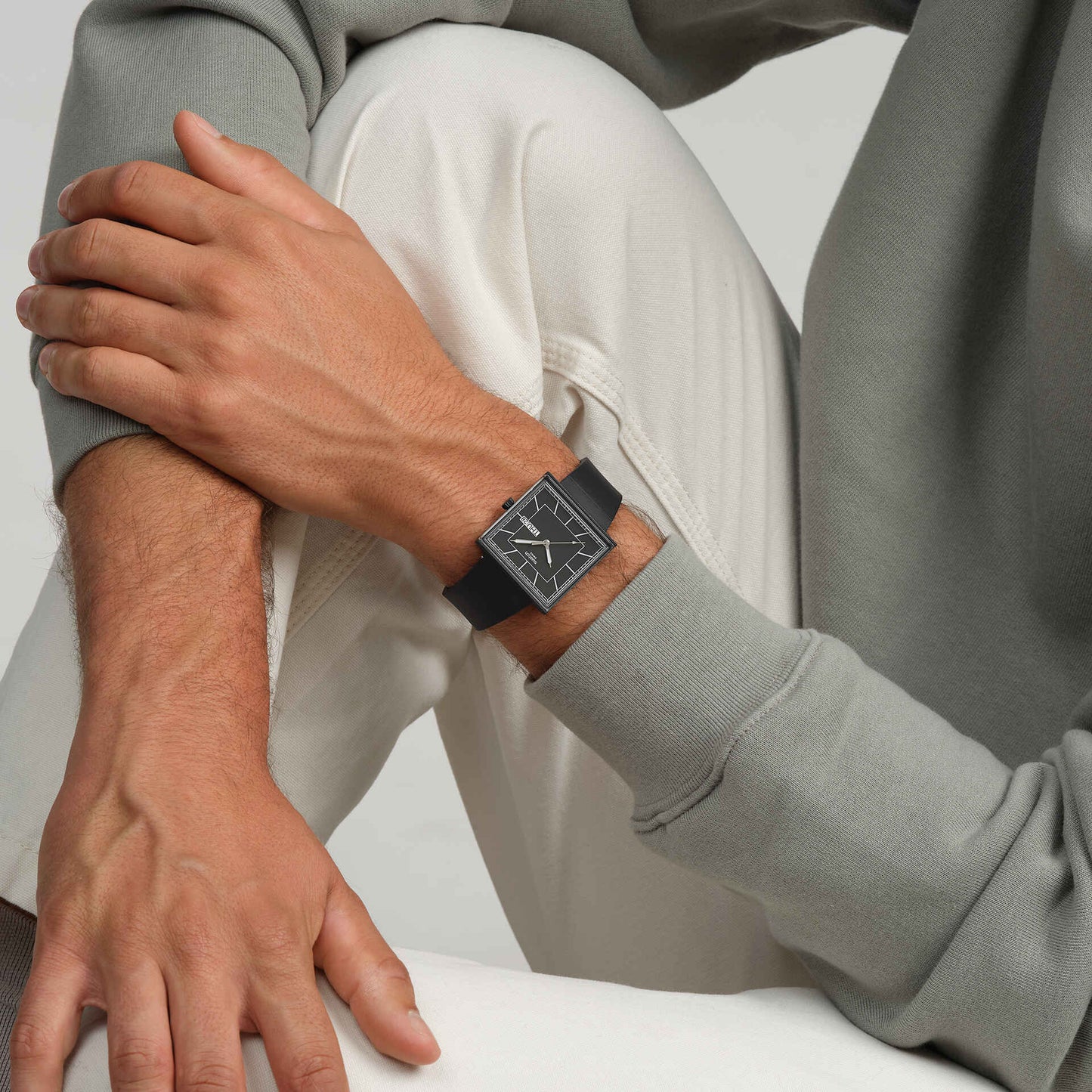 Herrenarmbanduhr Swatch am Handgelenk mit schwarzem Armband und quadratischem Zifferblatt