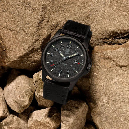 Montre pour homme sur des rochers : cadran noir, aiguilles argentées et bracelet noir
