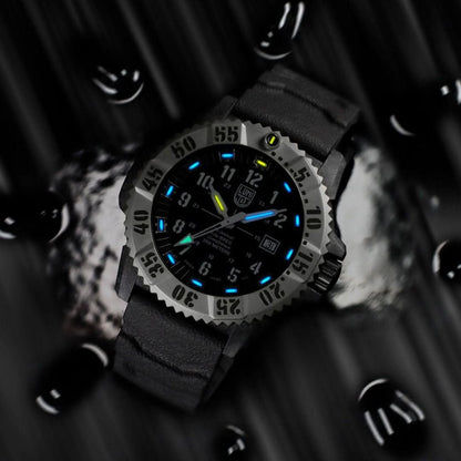 Montre homme avec boîtier gris et cadran noir, index luminescents bleus et verts.