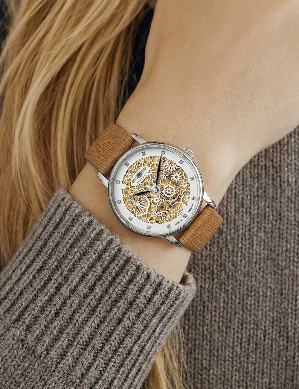 Damenarmbanduhr am Handgelenk: beiges Lederband, Skelett-Automatik, silbernes Gehäuse, goldene Details