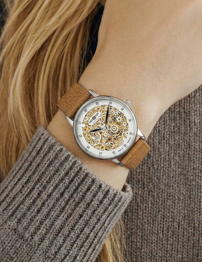 Damenarmbanduhr am Handgelenk: beiges Lederband, Skelett-Automatik, silbernes Gehäuse, goldene Details