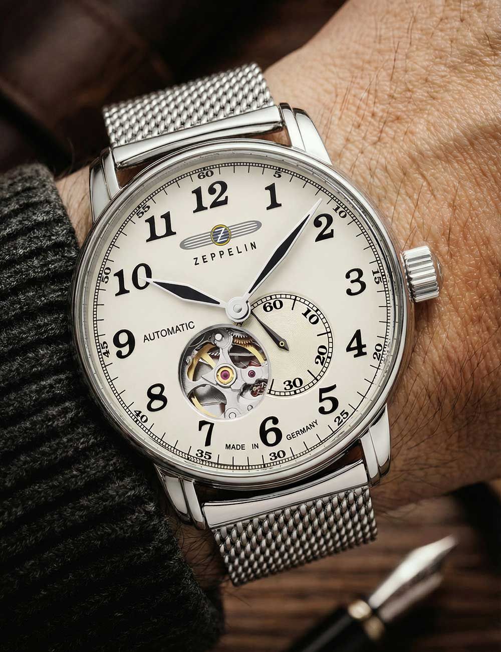 Zeppelin Herrenuhr am Handgelenk: silbernes Meshband, helles Zifferblatt, offenes Herz
