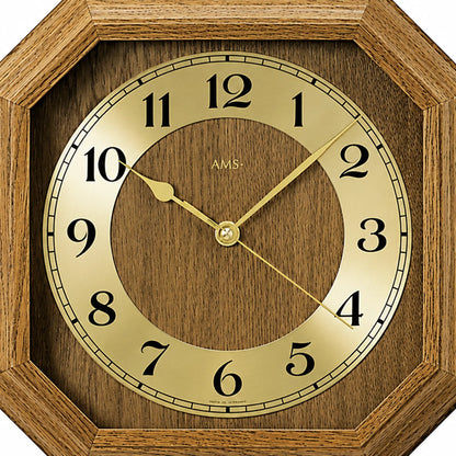 Nahaufnahme Wanduhr: Ziffernring, goldfarbene Zeiger und AMS-Schrift im eichen Holzrahmen