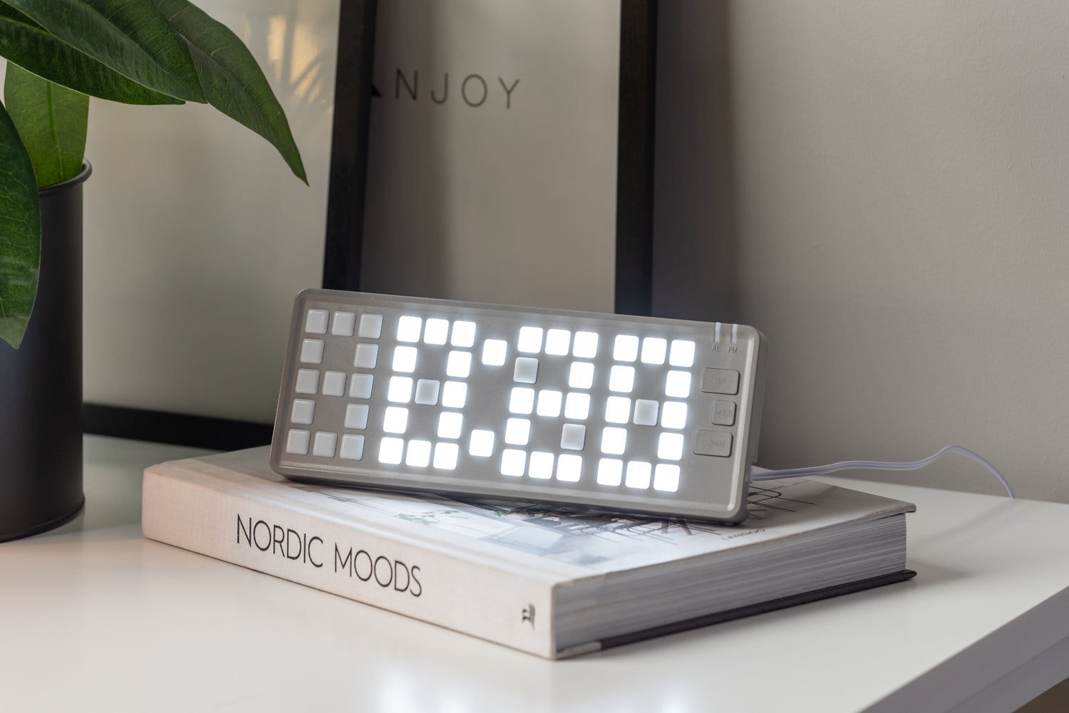 Retro-väckarklocka med tangentbordsdesign och lysande LED-display, ljusgrå, står på en hylla.