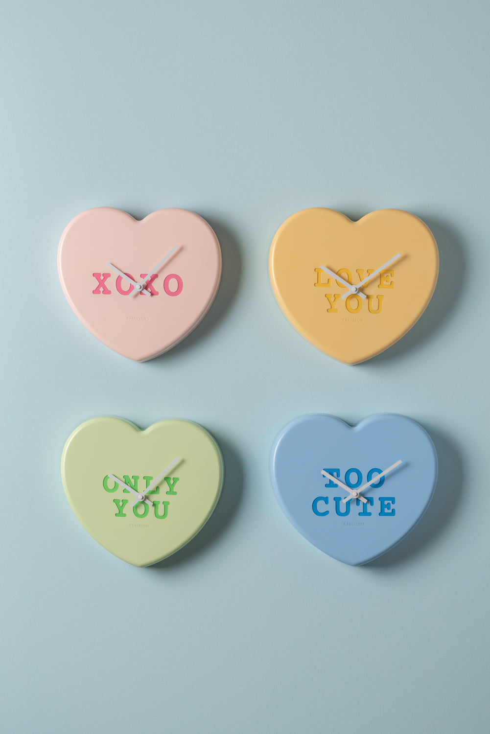 Fyra hjärtformade väggklocksdesigner i pastell: xoxo, love you, only you, too cute.