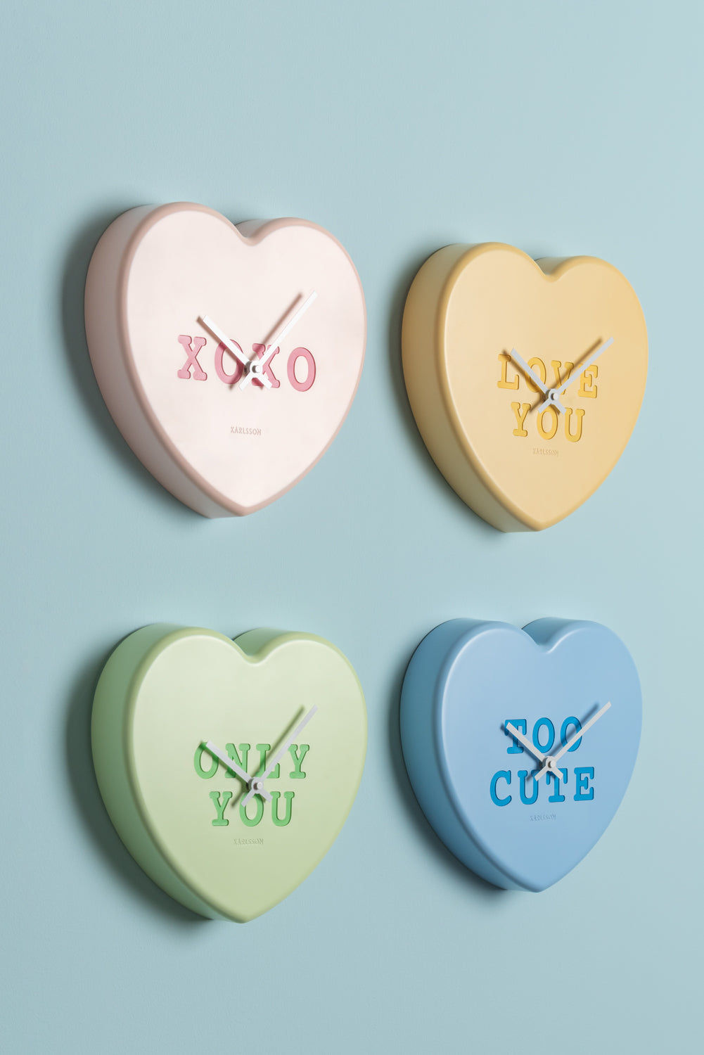 Fyra hjärtformade väggklocksfronter med XOXO-/du-du-tryck i kräm, gult, grönt, blått