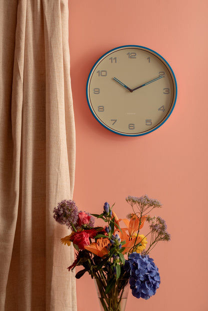 Rund väggklocka med ljusblå kant, vita siffror och metallvisare