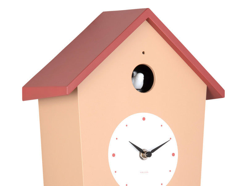 Väggklocka i form av ett litet hus: beige front, rött tak, rund urtavla och fågelöppning