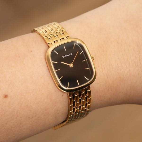 Damklocka på handleden: guldfärgat metallarmband med svart urtavla och visare