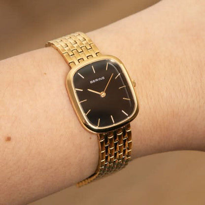 Damklocka på handleden: guldfärgat metallarmband med svart urtavla och visare