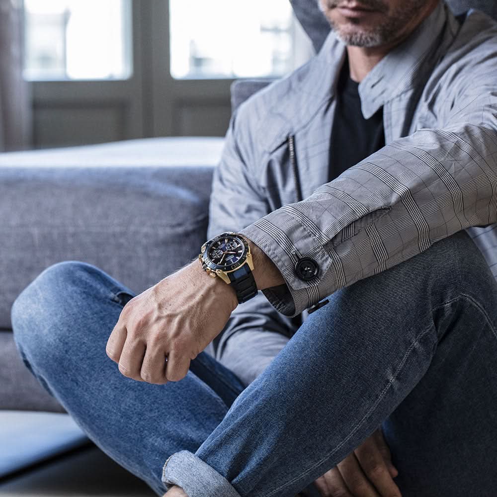Herrklocka på handleden med blått armband och blå-guldig urtavla