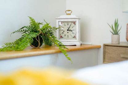 Vit bordsklocka med guldhandtag på locket placerad på en ljus träskiva