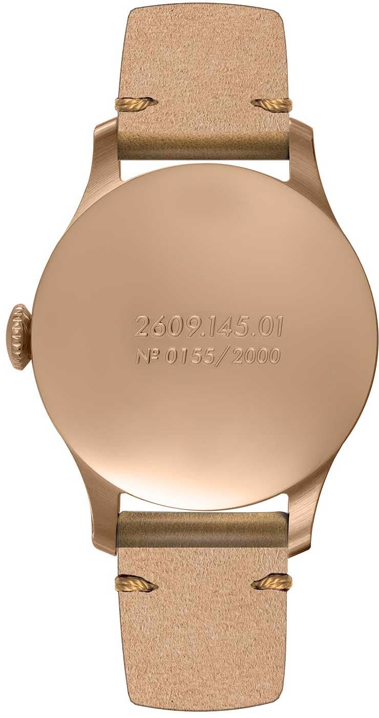 Baksida på analog klocka med brunt läderarmband, guldfärgat urverk och gravyr
