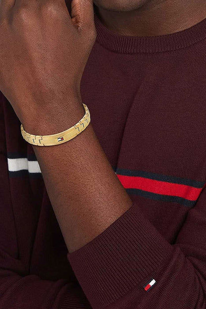 Gliederarmband med guldfärgade, texturerade länkar och liten logotyp vid handleden