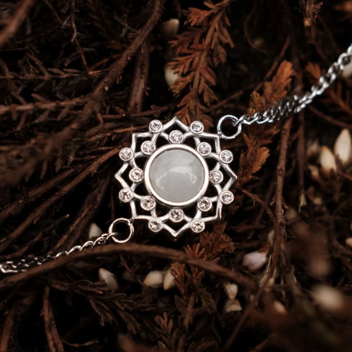 Silarmband med rund grå sten i blomsterornament och länkar.