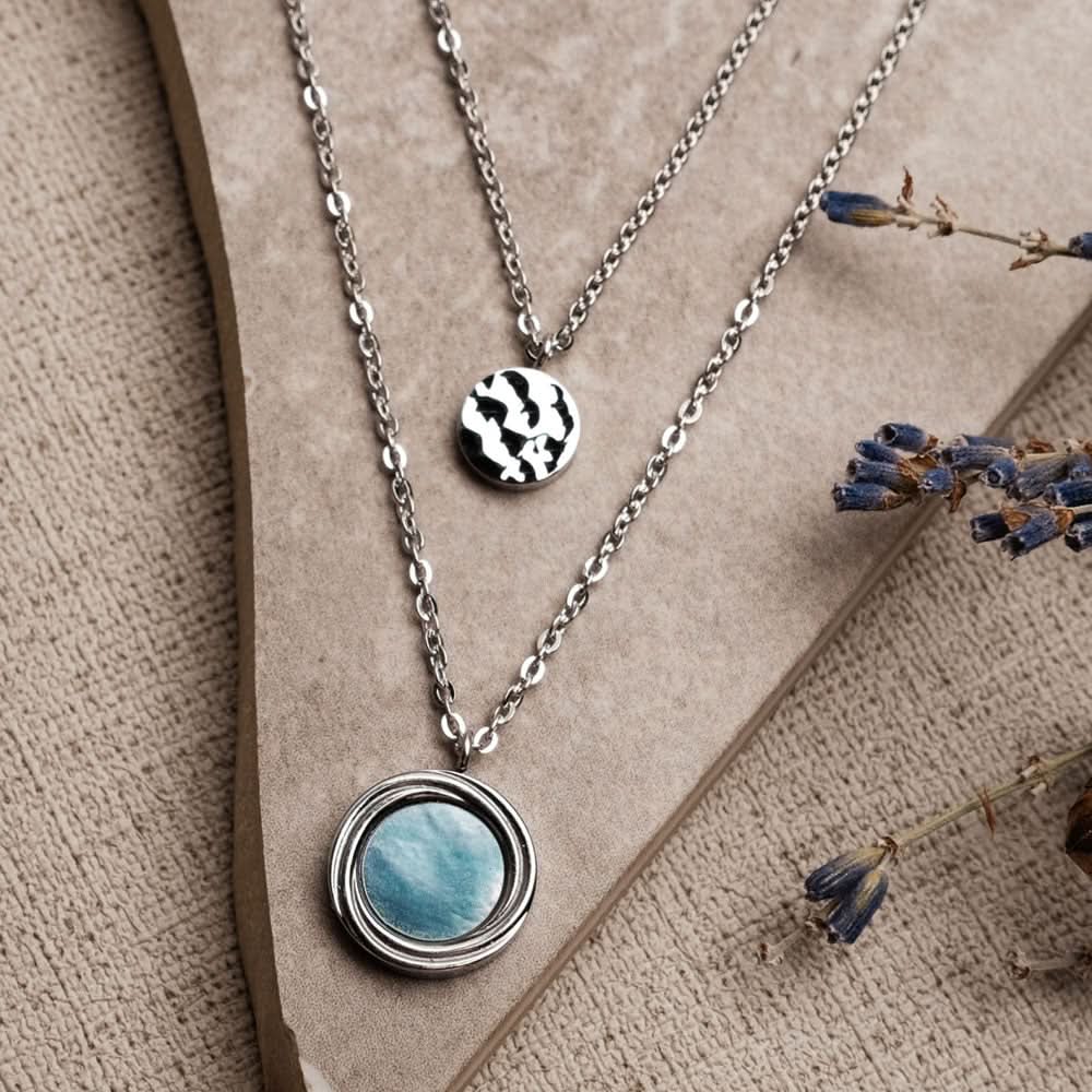 Lagerhalsband i silver med runt pärlemorhänge och en liten svartvit berlock