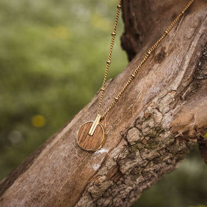 Halsband med rund träberlock och guldfärgat halsband vid trädstammen