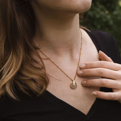 Halsband runt halsen: guldfärgat halsband med runt trävedhänge framför svart topp