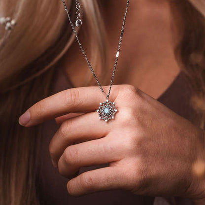 Silverfärgat halsband med snöflingepärla och blå sten i handen
