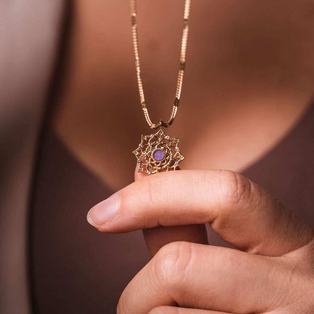 Fint halsband med guldfärgat hänge och lila sten i handen