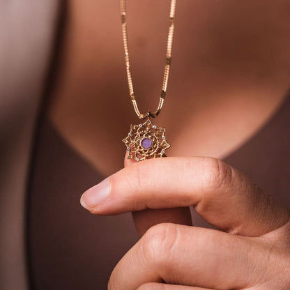 Fint halsband med guldfärgat hänge och lila sten i handen