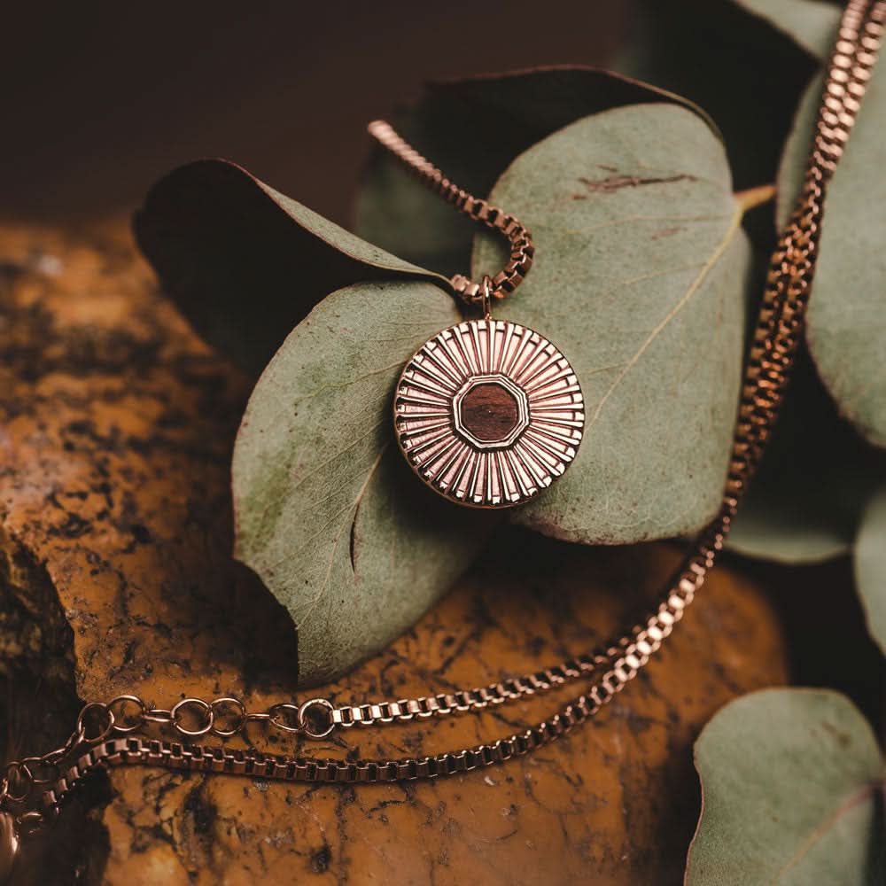 Halsband med rund metallberlock, strålmönster och mörk mitt på löv.