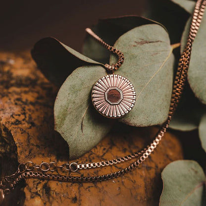 Halsband med rund metallberlock, strålmönster och mörk mitt på löv.
