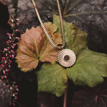 Halsband med rund berlock och strålrelief på blad, fin metallkedja.