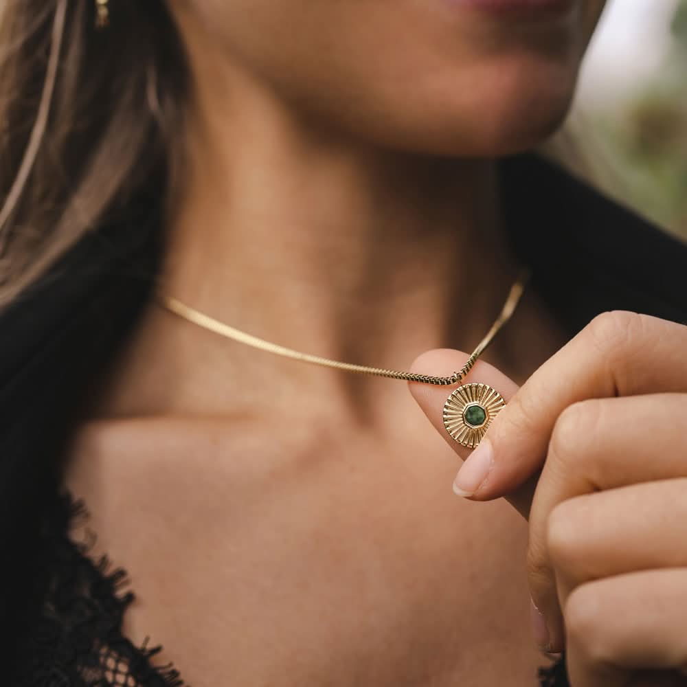 Gyllene halsband med rund berlock och grön sten, nära låset