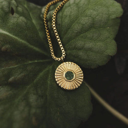 Gyllene halsband med rund berlock och grön sten, framifrån