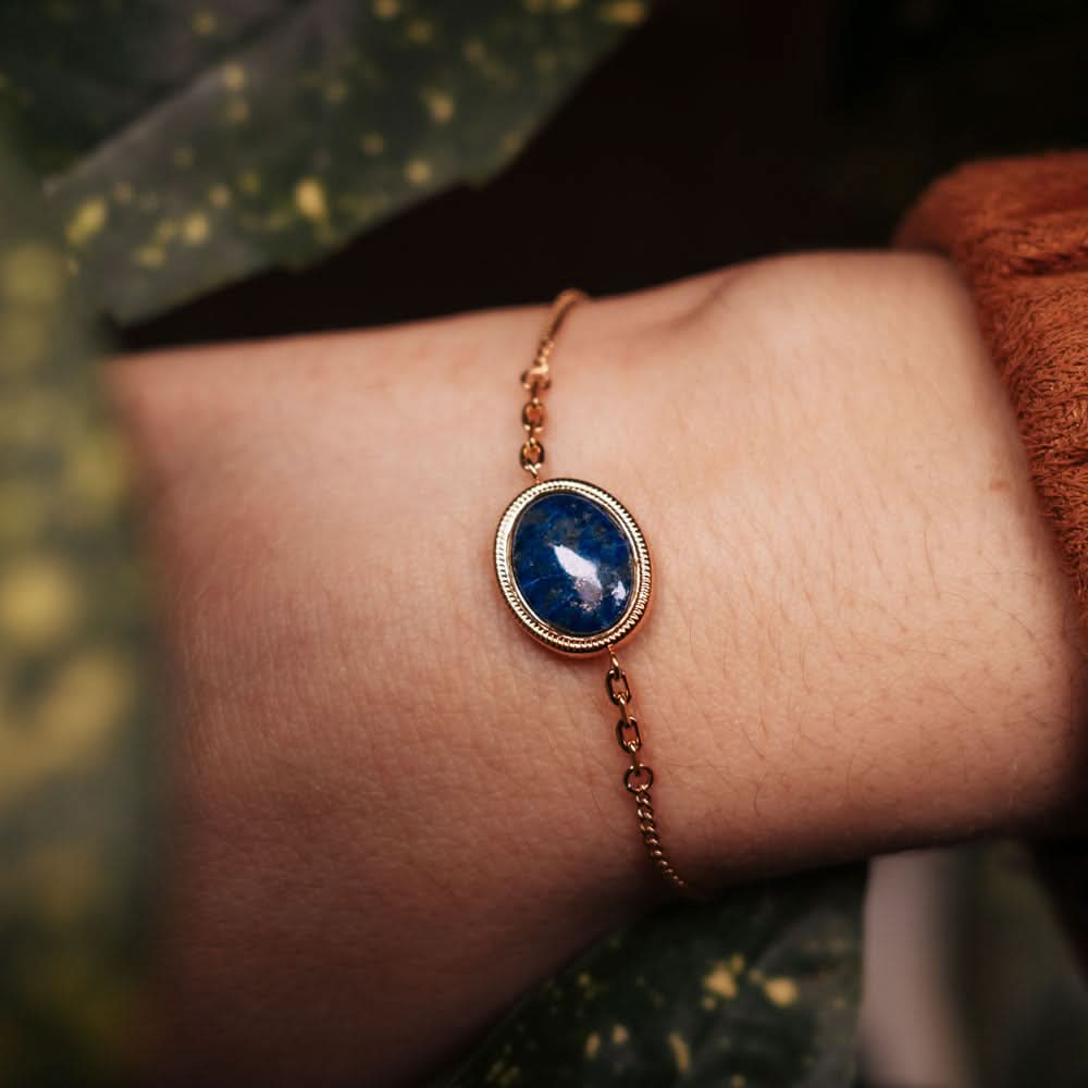 Guldpläterat armband med oval blå cabochonberlock vid handleden