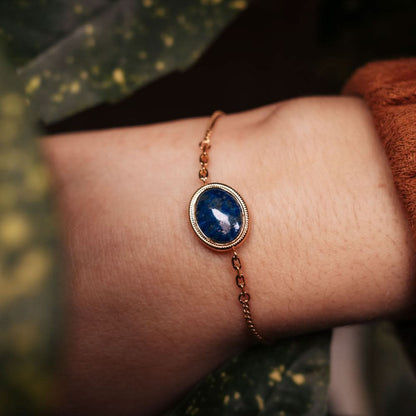 Guldpläterat armband med oval blå cabochonberlock vid handleden