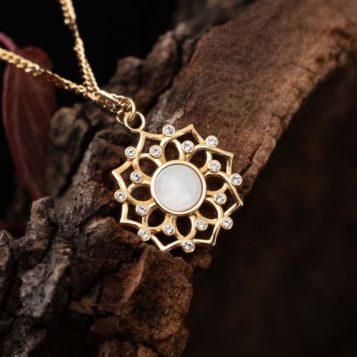 Guldhalsbandshänge med rund, vit cabochon och stenprydd solhjulsdesign