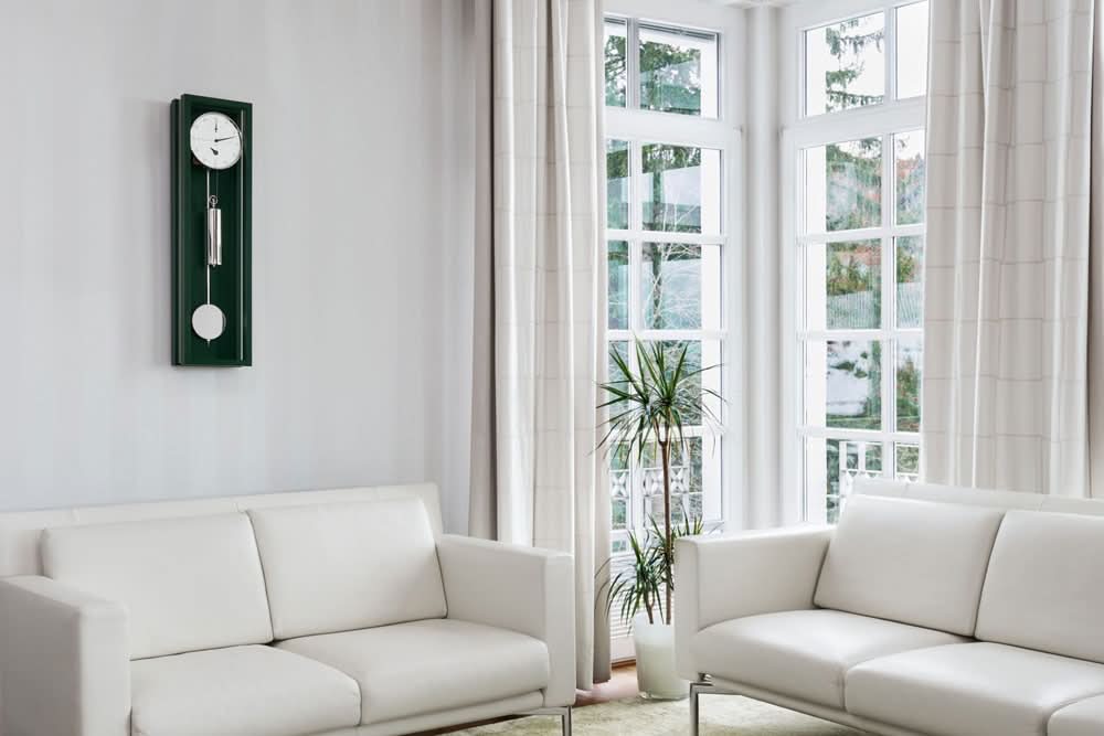 Grön väggklocka med rund urtavla, silverfärgad pendelupphängning och vit kulpendel