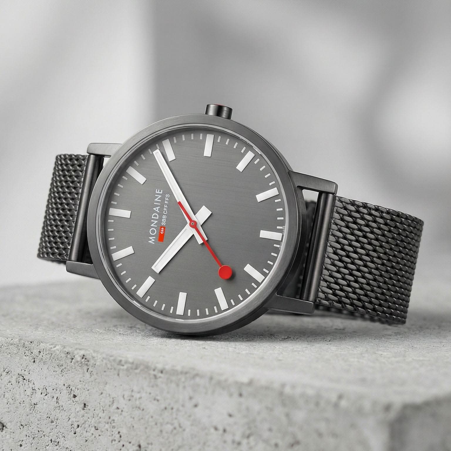 Mondaine herrur snett: grå urtavla, vita index, svart mesh-armband