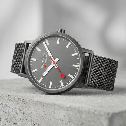 Mondaine herrur snett: grå urtavla, vita index, svart mesh-armband