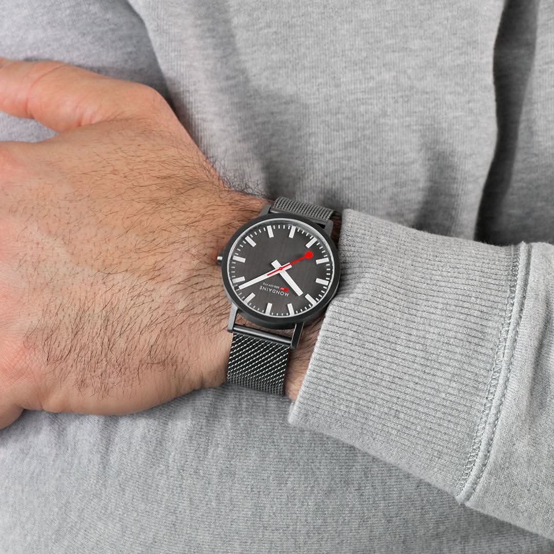 Mondaine herrklocka på handleden: svart mesh-armband och mörk urtavla