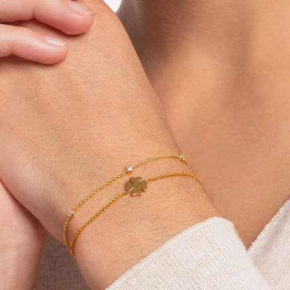 Guldpläterat armband runt handleden med vita stenar och ett litet hänge