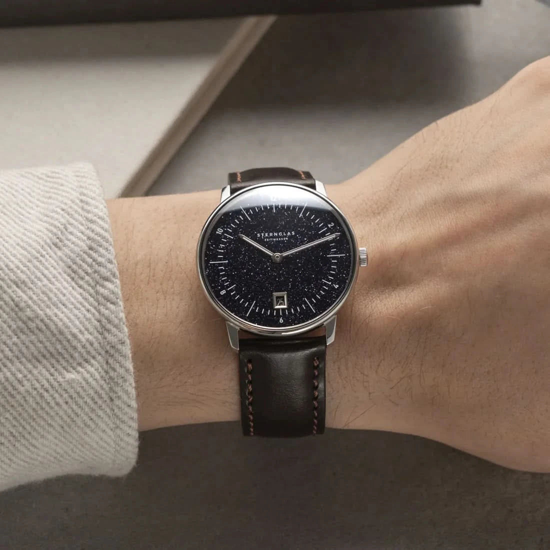 Armbandur på handleden med svart läderband och mörk urtavla
