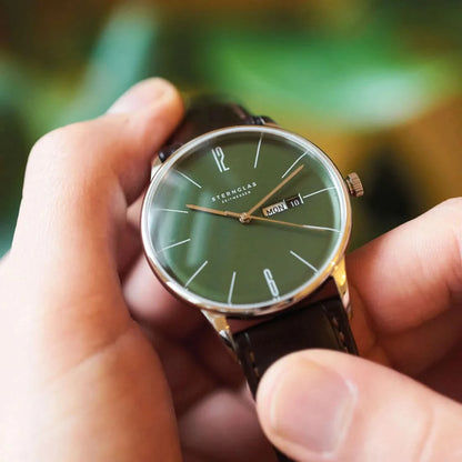 Unisexklocka i handen: grön urtavla, brunt läderarmband och datum vid klockan 10.