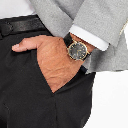 Armbandsur på handleden: guldfärgat hölje, mörkgrå urtavla och svart läderband