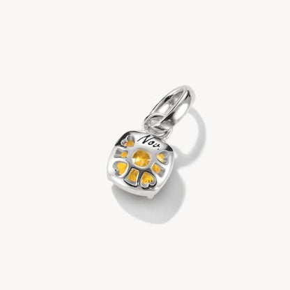 Silversmycke med texten "Nov", blomstermönster och gula stenar