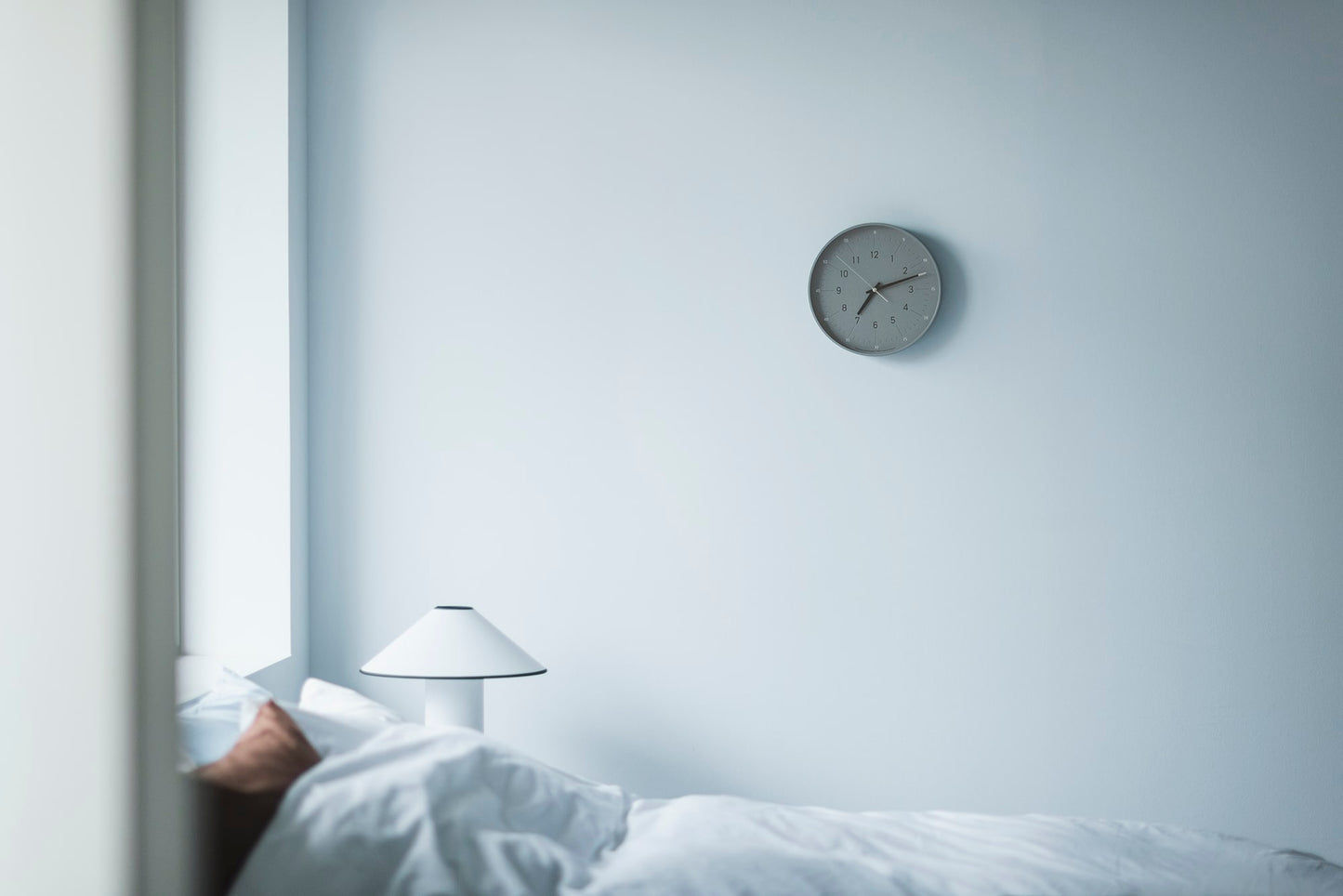 Kleine graue Wanduhr an der Wand über einem Bett