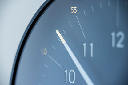 Detail einer runden Wanduhr: dunkelblaues Zifferblatt, weiße Zeiger, goldene Akzente