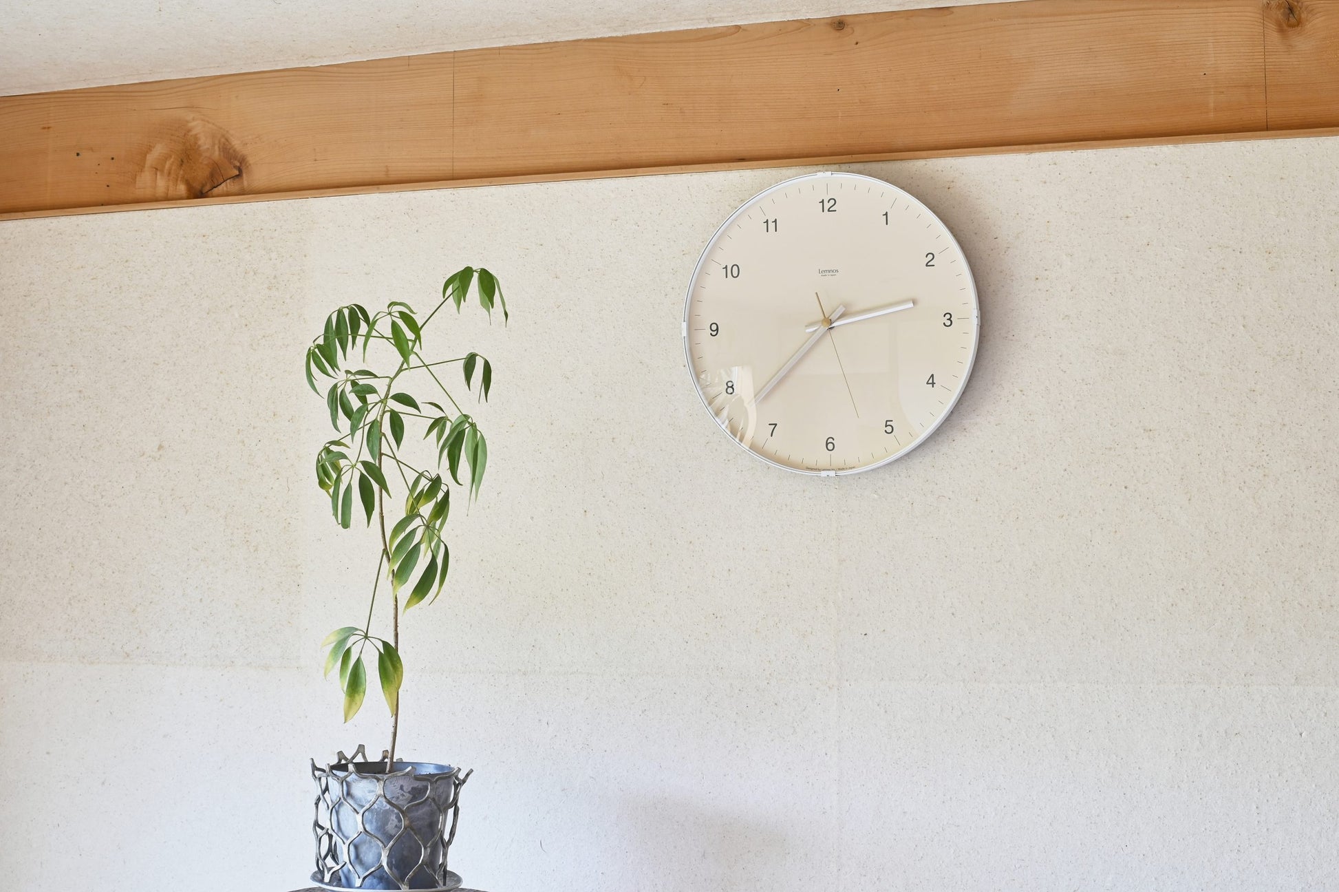 Beige Wanduhr an der Wand, silberner Rahmen und Metallzeiger auf Kuppelglas