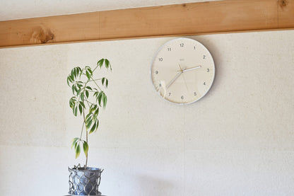 Beige Wanduhr an der Wand, silberner Rahmen und Metallzeiger auf Kuppelglas